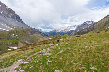 Hikers climbing uphill on steep rocky mountain trail. Summer adventures and exploration on the Alps. Dramatic sky with storm clouds.