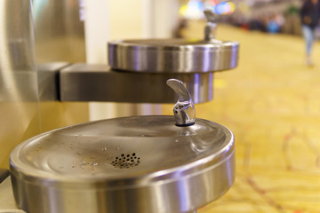close up of stainless steel public faucet with blurred airport terminal background.