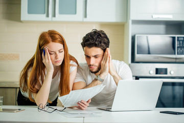 Worried couple paying their bills online with laptop at home in the living room