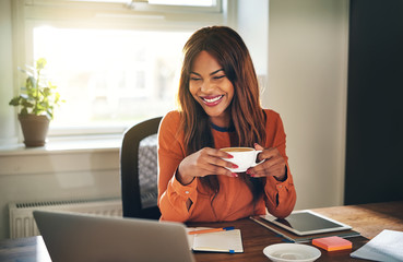 Laughing young woman drinking coffee while working from home