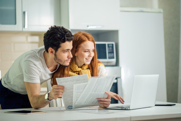 cheerful young couple calculating their bills at home