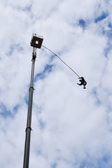 Fototapeta na wymiar Bungee juming - seen from the ground silhouette of a young man rushing down from a high crane platform