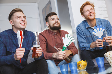 Men watching sport on tv together at home holding noisemakers