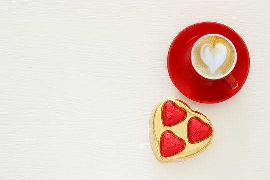 Valentine's day background. red cup of coffee with heart shape foam and chocolate. Top view image.