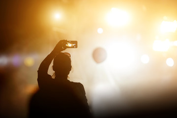 Silhouette of girl with a smartphone taking photo of concert stage.
