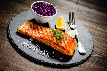 Grilled salmon with vegetables served on black stone plate on wooden table