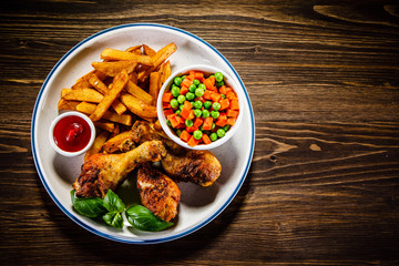 Grilled chicken legs with French fries and vegetables on wooden table background