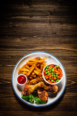 Grilled chicken legs with French fries and vegetables on wooden table background