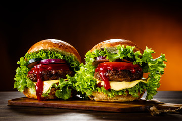 Two tasty burgers with cheese and ketchup served on cutting board - obrazy, fototapety, plakaty