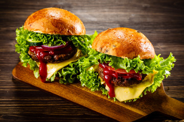 Two tasty burgers with cheese and ketchup served on cutting board