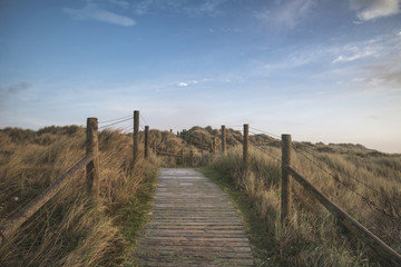 Fototapeta na wymiar Beautiful sunrise landscape image of sand dunes system over beach with wooden boardwalk
