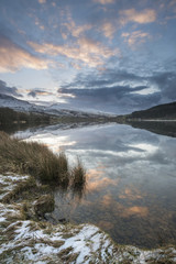 Stunning sunrise landscape image in Winter of Llyn Cwellyn in Snowdonia National Park with snow capped mountains in background