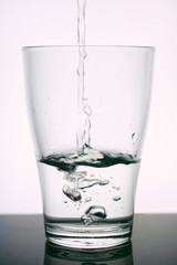 Glass beaker into which Water flows. Water is clean - glass is transparent. Glass on a white background. Water is pure ecology