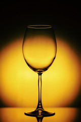 Wineglass on a yellow background with a black vignette. A tall Wineglass with a thin stalk. The Wineglass is empty, the background is blurred and ellegant