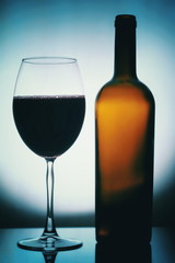 Glass and a Bottle of Wine. Bottle is open, half of it is Wine. Glass and Bottle of wine on a yellow background with a black vignette. Ellegant forms of Bottlr and Glass