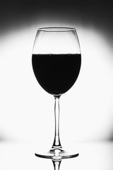 Glass for wine black and white photo with black vignette. A tall glass with a thin stem. The wine glass is half full, the background is blurred and elegant