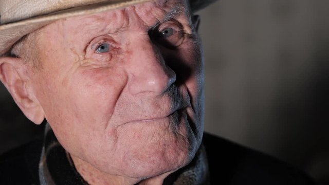 portrait of 92 years aged senior caucasian man with white hat looking at camera against white wall and smiling. Elderly Grandfather at home. Slow motion