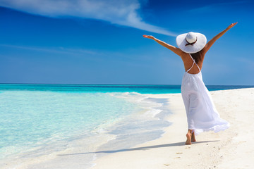 Attraktive Frau in weißem Kleid läuft an einem tropischen Strand und ist glücklich