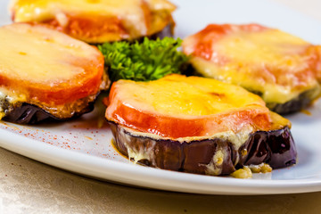 Eggplants baked with tomato and cheese on white plate