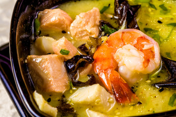 Asian seafood soup with spics and herbs in black bowl