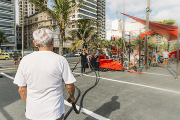 Older man (80-89) and mature woman (70-79) exercising with battling rope at public gym in Ipanema, Rio de Janeiro, Brazil