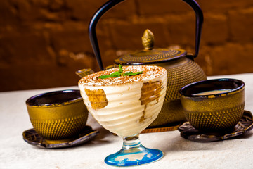 Indian masala chai, spiced tea with milk. Teapot, two cups and tiramisu - obrazy, fototapety, plakaty