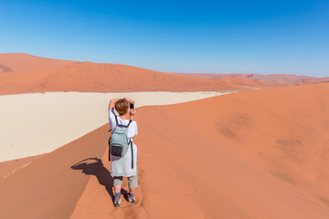 Tourist taking photo at Sossusvlei, Namibia. Scenic sand dunes, Namib desert, Namib Naukluft National Park, travel adventure in Africa.