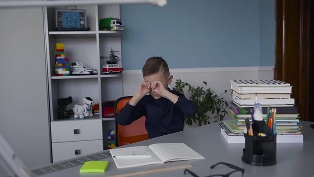 A boy is a schoolboy waking up at a table at which he did his homework. Tired child from homework. Books and notebooks on the table