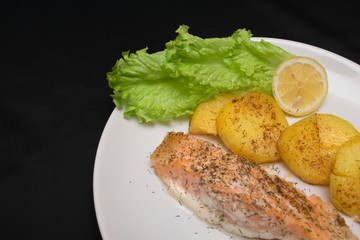 salmon fish fillet with fryed potato, lemon and fresh leaves of salad