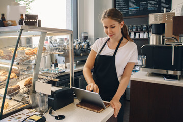 Portrait of young caucasian female woman cashier. Seller using touch pad for accepting client customer payment. Small business of coffee shop cafeteria.