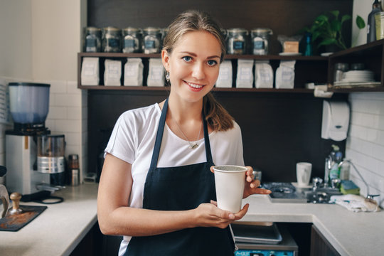 Young Caucasian barista hands holding paper cup with coffee. Small business and person at work concept