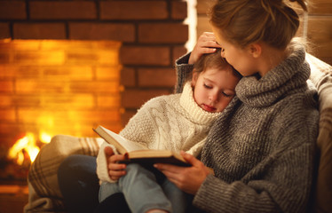 happy family mother and child daughter read book on winter evening near fireplace