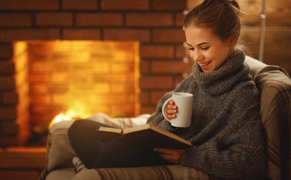 young woman   reading a book by the fireplace on a winter evening
