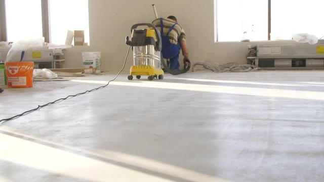 Workers in uniform cleaning room with a vacuum cleaner after installing wood parquet board during flooring work. Man vacuuming floor during repairs