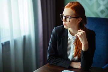 Pensive redhead young businesswoman using tablet computer in office, ginger woman thinking and holding pen and digital tablet
