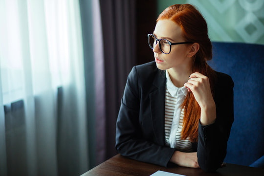 Pensive redhead young businesswoman using tablet computer in office, ginger woman thinking and holding pen and digital tablet