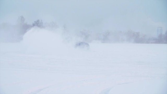 Car drives on a snowy road, slow motion. Car with winter tyres installed on light alloy wheels in snowy outdoors road. A car driving down a snowy road during winter