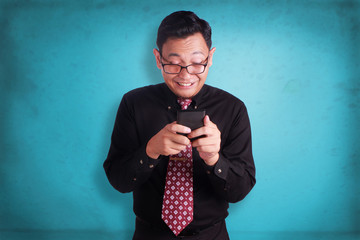 Young businessman reading text chat on his phone, happy smiling