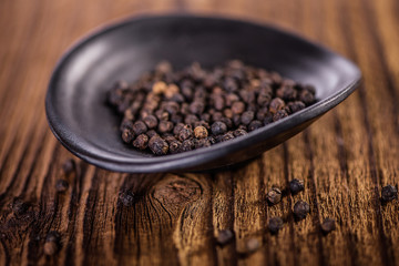 detail close up of whole black peppercorn in a black dish bowl  on wooden table