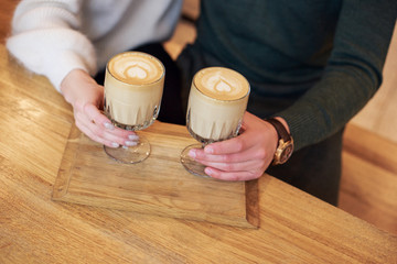 A boyfriend and a girlfriend are drinking coffee. A heart drawing on each cup on cappuccino.