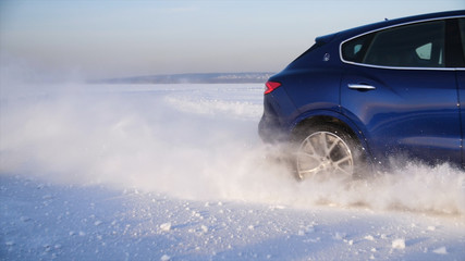 Car with winter tyres installed on light alloy wheels in snowy outdoors road. A car driving down a snowy road during winter. Car drives on a snowy road