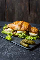 Croissant sandwich with tuna, hard boiled egg, salad and cucumber on stone table