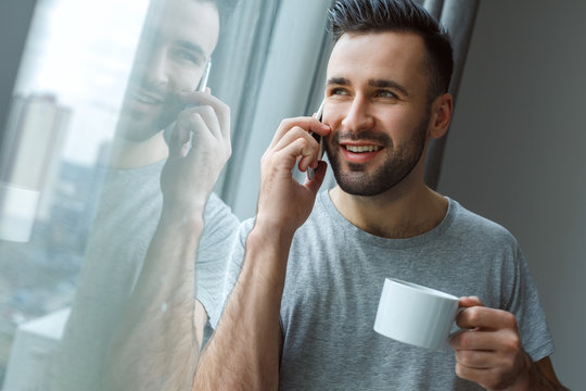 Bachelor man daily routine standing near the window single lifestyle concept drinking coffee phone call