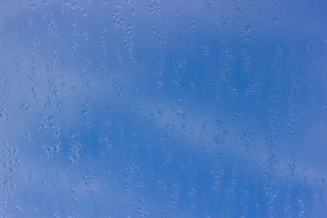 Droplets of rain water on dirty window, against blue with shallow DOF