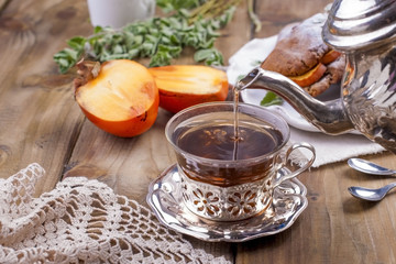 Homemade pastries with persimmons, for breakfast. Beautiful glass with tea. Kettle. Wooden table, tablecloth with lace. Free space for text or advertising.