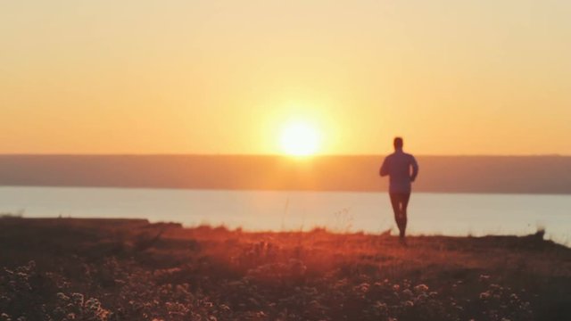 young man trail runner training outdoors in the fields, sunset in lake background 