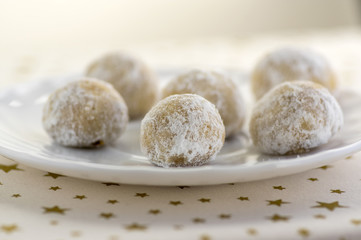 Fototapeta na wymiar Christmas cookies, tasty balls with hazelnut inside and icing sugar, white plate and tablecloth with golden stars