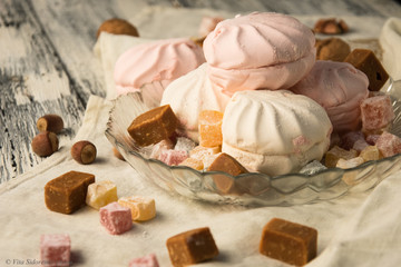 still life of sweets, marshmallows and candies in a glass vase on a wooden table