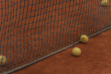 Tennis balls on red court with gray net