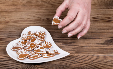 Female hand holding a beautiful sweet heart for good luck and white plate. Symbols of love, bond, marriage or friendship on a brown wood background.